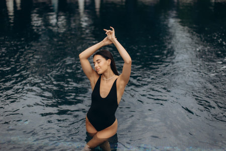 Tourist relaxing in a swimming pool, eyes closed and arms raised, soaking up the summer sun while...