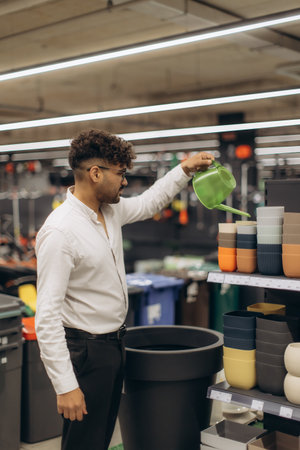 A man browsing in a store, exploring gardening tools and pots, holding a green watering can. The scene reflects leisure, shopping, and interest in gardening supplies inside a neatly arranged store.の写真素材