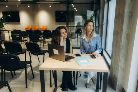 Two professional women collaborating at a desk in a spacious office environment, exemplifying teamwork, productivity, and modern workspace design.の写真素材