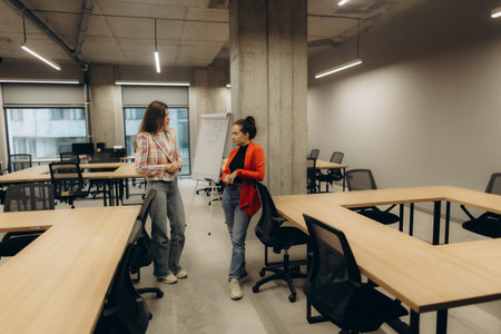 A workspace featuring two individuals engaged in a discussion. Modern office furniture surrounds...
