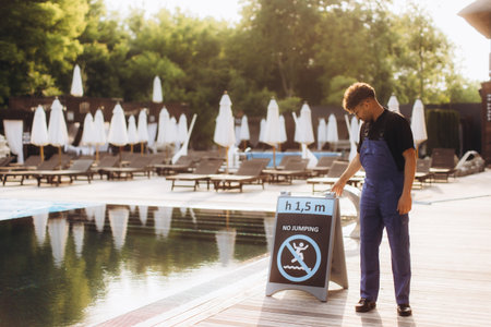 Pool attendant positioning a no jumping sign at the edge of a resort swimming pool, ensuring guest safetyの写真素材