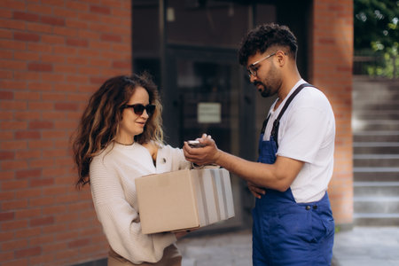 Courier delivering a package to a customer while processing payment through a mobile phone, highlighting modern e-commerce and logisticsの写真素材