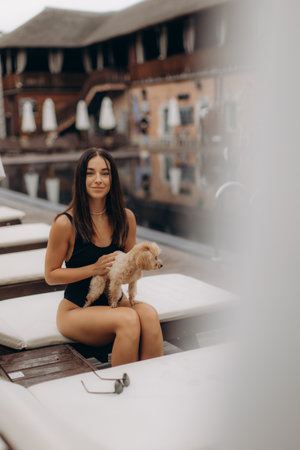 Tourist relaxing by the pool with her adorable poodle, soaking up the sun and enjoying a blissful vacation at a luxurious resortの写真素材