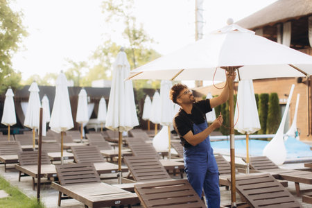 Hotel worker setting up parasol by the pool, preparing the resort for guests during summer seasonの写真素材
