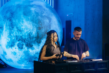 A male and a female DJ collaborate on a music set against a surreal moon-themed background,...