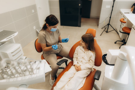Pediatric dentist wearing mask and gloves showing dental instruments to little girl sitting in dentist chairの写真素材