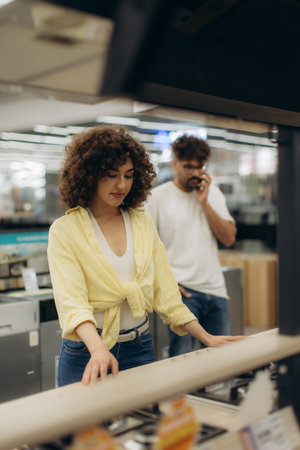 A scene in an electronics store involving two individuals browsing items on display. The atmosphere conveys modern shopping dynamics and decision-making processes.の写真素材
