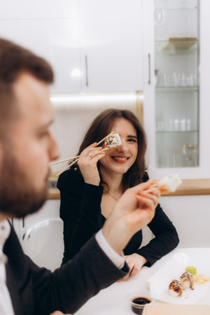 Two people engaging in a joyful moment enjoying sushi at home, laughing and connecting. The casual meal emphasizes friendship, joy, and the pleasure of sharing experiences together in an inviting home environment.の写真素材