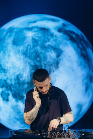 A DJ operates a turntable in an atmospheric setting with a glowing lunar backdrop, creating a vibrant and engaging musical experience. The scene conveys energy, creativity, and nightlife culture.の写真素材