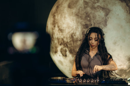 Woman DJ creating music on a mixer wearing headphones, with a moon-themed backdrop. Creative and artistic atmosphere illustrating nightlife, creativity, and passion for music showcasing a distinctive style.の写真素材