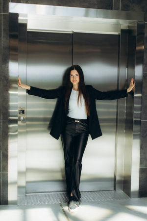 A professional woman confidently leans against an elevator in fashionable attire, showcasing determination and style in a modern setting.の写真素材