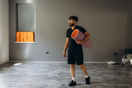 Man standing in studio, holding yoga mat, preparing for fitness exercise, practice, or healthy lifestyleの写真素材