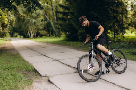 Man riding a bicycle on a paved path in a lush green park, enjoying outdoor leisure and active lifestyleの写真素材