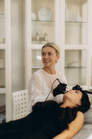 Beautician wearing gloves applying permanent lip liner to woman in beauty salon, focusing on cosmetic enhancementの写真素材