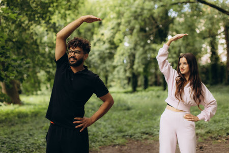 Couple performing side stretches in a green park, focusing on wellness and a healthy lifestyle outdoorsの写真素材