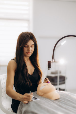 Woman cosmetologist practicing led eyelash extensions on a mannequin head using specialized tools and an led lampの写真素材