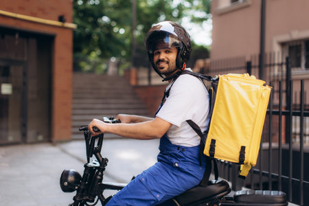 Courier wearing helmet and yellow thermal backpack riding electric scooter delivering food in the cityの写真素材