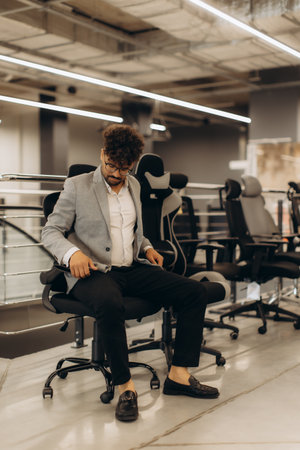 A man in a professional setting evaluates various ergonomic office chairs, seated professionally to determine comfort and aesthetics, representing workplace ergonomics, modern office furniture, and business facility settings.の写真素材