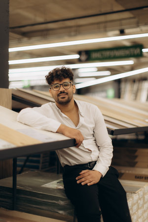 A man dressed in formal attire leans against a display table in a well-lit store. The image conveys a professional yet casual vibe in a modern retail setting.の写真素材