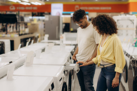 A man and a woman examine washing machines while considering their options in an electronics store.の写真素材