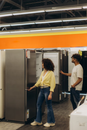 A couple examines a modern refrigerator in an electronics store. The brightly lit showroom displays various appliances for sale, offering a shopping experience that combines functionality and style.の写真素材