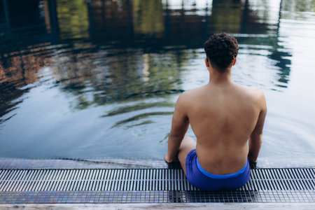 Rear view of a male swimmer resting at the edge of a pool after a workout, enjoying the tranquility of the waterの写真素材