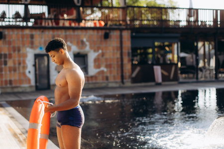 Young lifeguard holding a lifebuoy, ensuring safety and vigilance by the pool on a sunny summer day, ready for any rescue situationの写真素材