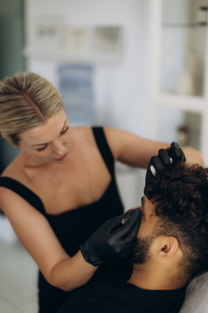 Beautician applying permanent eyebrow makeup to a man's brow, enhancing his appearance and giving him a defined lookの写真素材