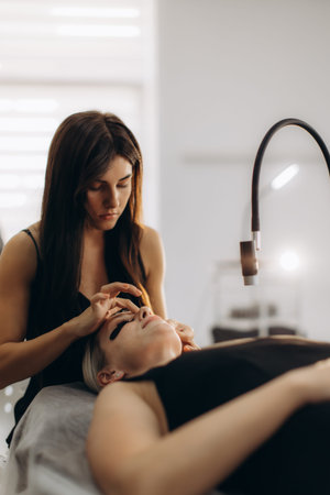 Professional beautician applying eyelash extensions to female client in a modern beauty salon, using...