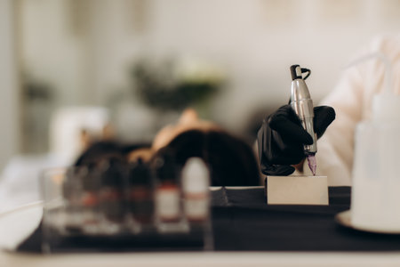 Professional hand in black glove holding tattoo machine, preparing for permanent cosmetic makeup procedure in beauty salonの写真素材