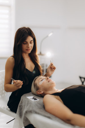 Skillful beautician applying led eyelash extensions to a female client's eyes at a modern beauty salonの写真素材
