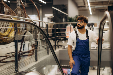 Man in workwear descending an escalator at a department store, reflecting a retail environment with various productsの写真素材