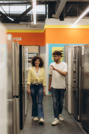 A couple walks through an electronics store, browsing refrigerator options. The store features bright lighting, modern appliances, and a spacious layout, offering a pleasant shopping experience.の写真素材