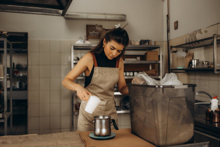 Woman in an apron accurately weighing wax flakes into a melting pot on a digital scale for craft candle productionの写真素材