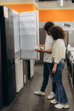 A young couple examines a refrigerator unit's storage and design features in a modern electronics retail store, evaluating their options.の写真素材