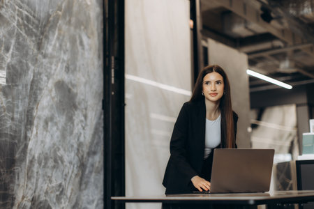 Confident businesswoman using a laptop in a stylish, contemporary office space. The image conveys professionalism, focus, and a modern work setting with sleek architectural backgrounds.の写真素材