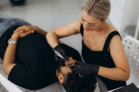 Beautician applying permanent eyebrow makeup to a male client in a beauty salon, symbolizing male grooming and aesthetic proceduresの写真素材
