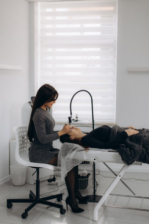 Specialist beautician applying artificial eyelashes to a woman client during a professional beauty treatment in a salonの写真素材