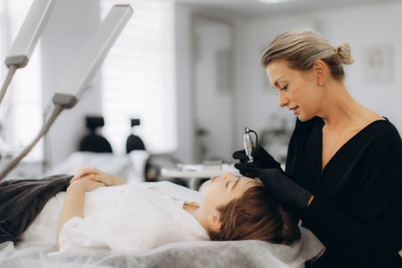 Beautician performing cosmetic microblading on a young woman's eyebrows in a beauty salon, enhancing...