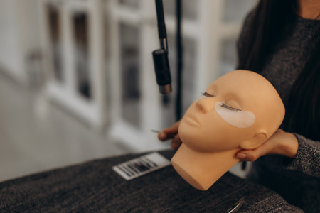 Beautician holding a mannequin head with eye patches and false lashes applied, training for eyelash extension procedureの写真素材