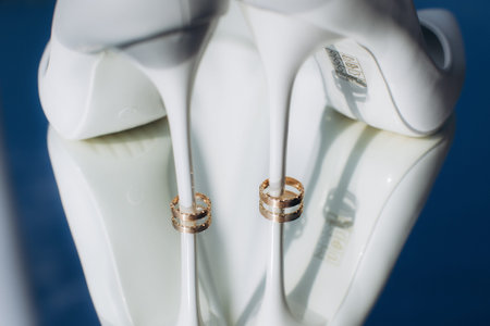 Gold wedding rings hanging gracefully on the stiletto heels of elegant white bridal shoes,...