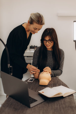 Instructor helping student practice applying individual eyelash extensions on a mannequin head...