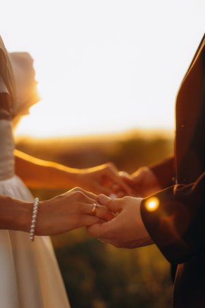 Bride and groom holding hands, showing wedding rings during a romantic outdoor ceremony at golden hourの写真素材