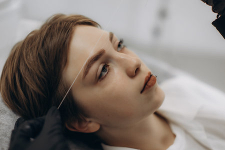 Woman receiving professional eyebrow threading service at a beauty salon, focusing on hair removal for perfect brow shapingの写真素材