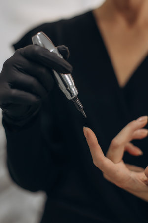 Professional beautician in black gloves holding a microblading pen, preparing for a permanent makeup...