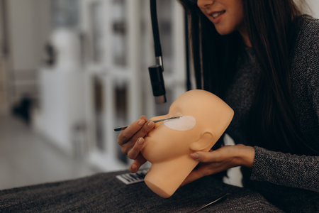 Female beautician hands applying eyelashes on a training mannequin head during an extension course in a beauty salonの写真素材