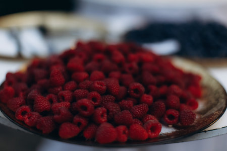 Freshly picked red raspberries piled high on a dark brown plate. A delicious, healthy snack or...