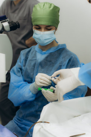 Medical professionals in sterile uniform and masks using specialized equipment for a delicate procedure in a healthcare environmentの写真素材