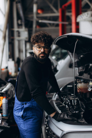 Young man mechanic in overalls inspecting a car engine, providing professional auto repair and maintenance serviceの写真素材