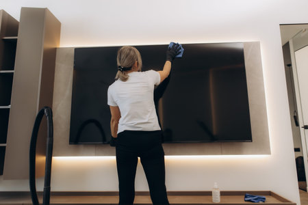 Woman cleaning a modern tv screen with a microfiber cloth and protective gloves, ensuring hygiene and maintenance in a living roomの写真素材